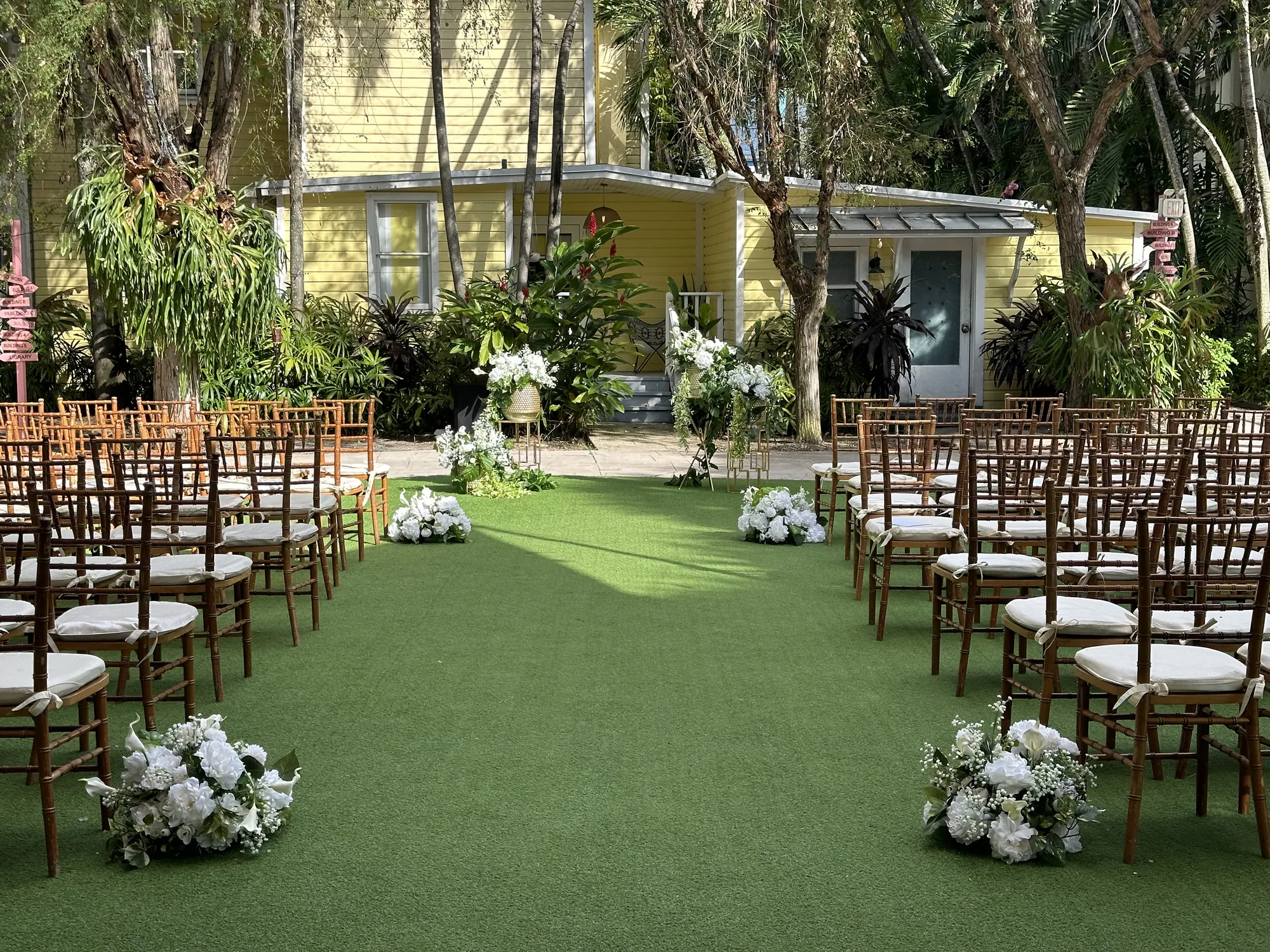 A ceremony set up on the lawn - rows of chairs and white flowers down the aisle, the houses behind