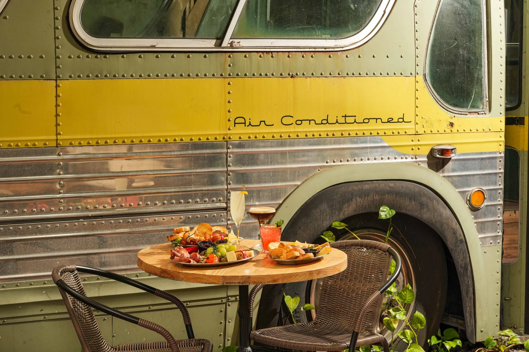 The side of the vintage bus - riveted steel, a yellow stripe and Air Conditioned in script - with a table set beside it