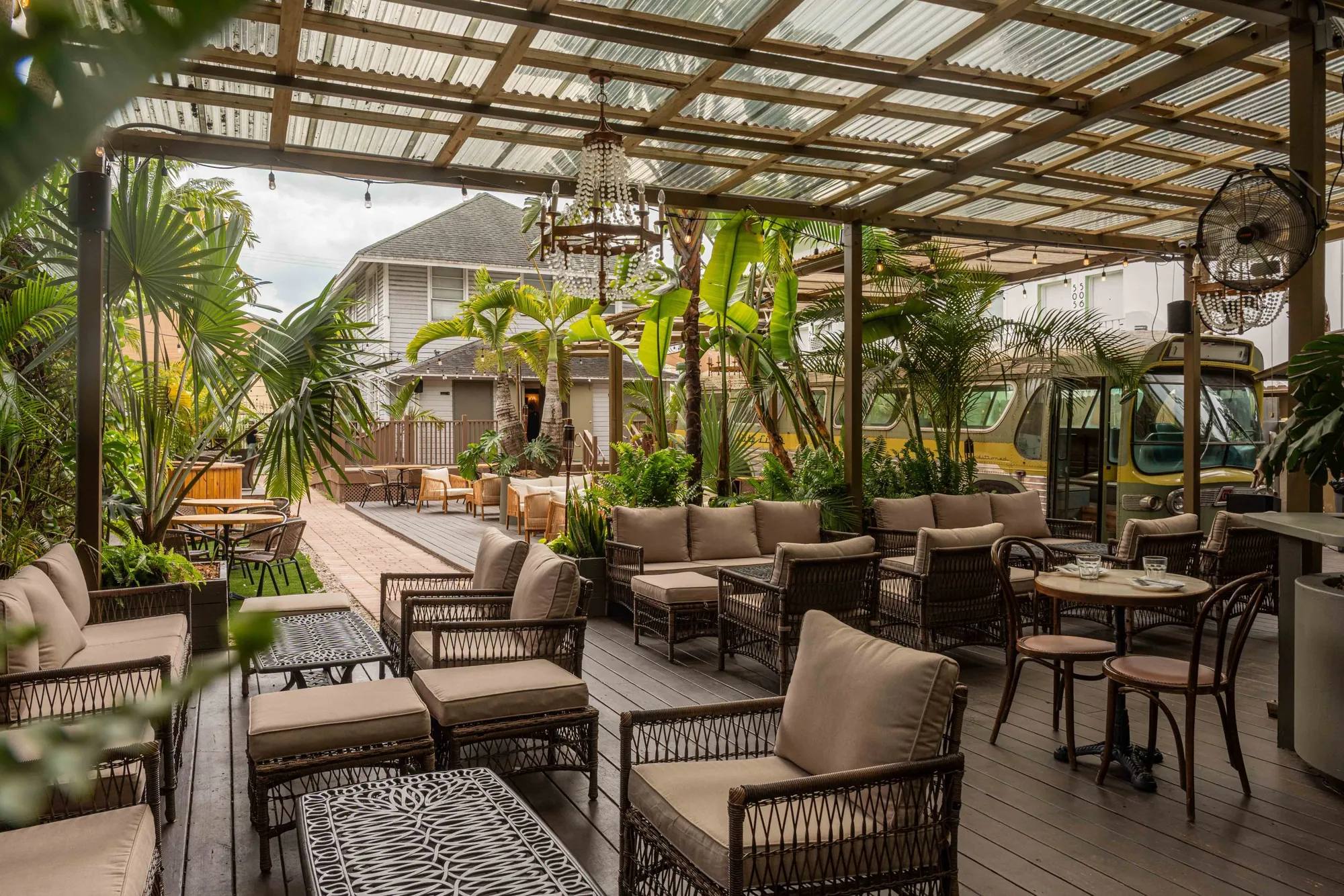 The garden patio at dusk - chandeliers and string lights under a pergola, palms behind