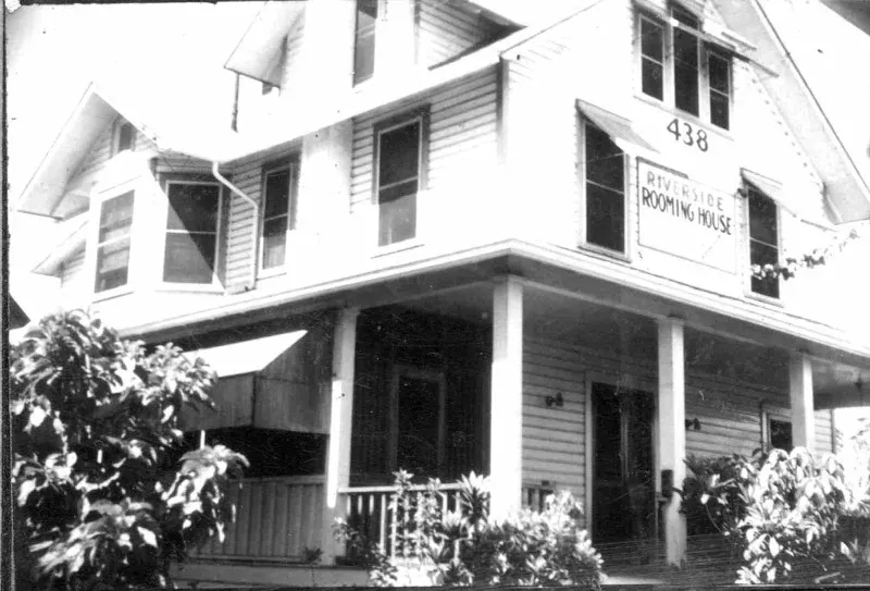 Black-and-white photograph of one of the houses, its double porch and palms